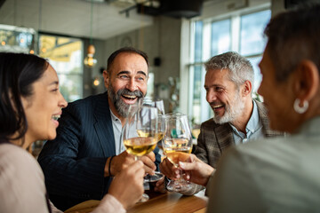 Mature adult friends laughing and toasting with wine in a restaurant
