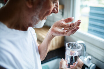Senior man taking medication at home kitchen, focused