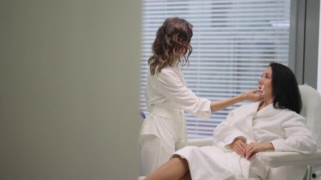 Professional cosmetologist discussing beauty procedure with female patient relaxing in chair, marking face with pencil for future cosmetic treatment in modern aesthetic clinic. Concept of anti-aging.