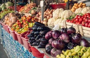 A vibrant assortment of fresh vegetables arranged in baskets at a market. The display includes eggplants, peppers, tomatoes, and more, showcasing a variety of colors and textures.