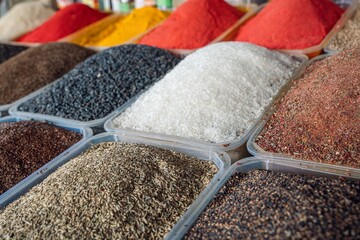 An array of colorful spices and herbs displayed in containers, showcasing vibrant textures and hues, perfect for culinary use or food photography.