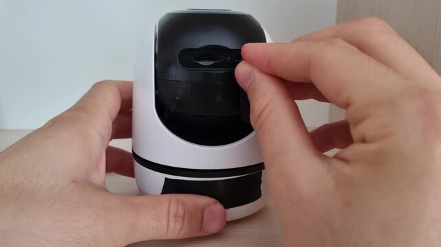 Close up of a hand using a pin tool to press and hold the factory reset button on a smart security camera to restore default settings