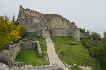 Footpath leading uphill to the massive stone walls and ruins of Eisenberg Castle under a gray sky.
