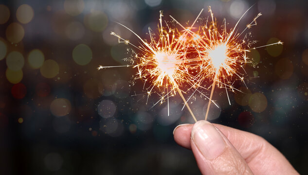 two burning sparklers between fingers and colorful bokeh in the background