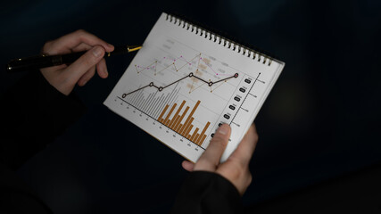 A close-up view of hands holding a notepad filled with graphs and charts, illustrating data trends...