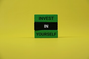 three colorful wooden blocks spelling 'Invest In Yourself' against a bold yellow backdrop. Perfect for themes of self-improvement, motivation, and personal growth in wellness and education materials.
