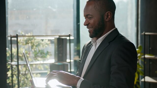 Smiling ethnic man African American businessman business agent with laptop in corporate office adult male executive professional working online working digital data analysis review browsing computer