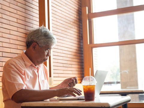 Concentrated senior Asian man holding a credit card while using a laptop for online shopping or banking at a cafe. Active elderly person showing digital literacy and independence in retirement.