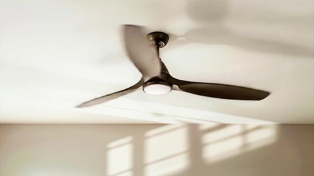 Minimal elegance in motion&mdash;sleek ceiling fan casts soft shadows across sunlit white ceiling and modern interior.