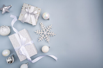 Elegant silver Christmas presents surrounded by frosted pine, baubles, and ribbons on a light blue...