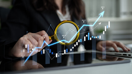 A business professional examines financial growth charts with a magnifying glass, showcasing market trends and modern data visualization in a sleek office environment. Scalp