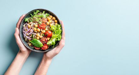 Hands holding a bowl of fresh quinoa salad with vegetables and chickpeas; healthy eating concept.