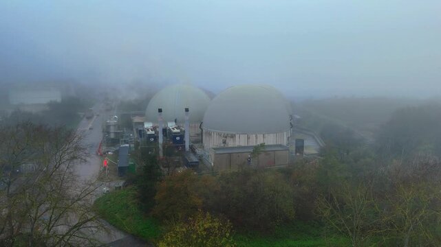 Aerial view of two dome-shaped structures shrouded in a dense fog, contrasting with the surrounding muted greenery, Bury Saint Edmunds, England, United Kingdom.