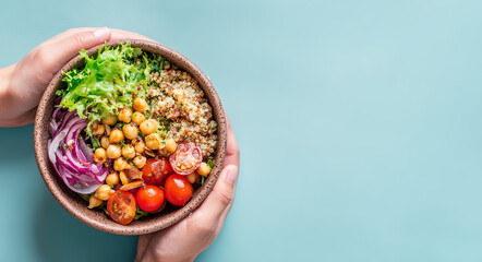 Hands holding a bowl of fresh quinoa salad with vegetables and chickpeas; healthy eating concept.