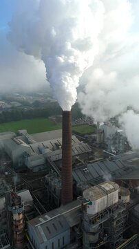 Aerial view of billowing white smoke rising from a tall brick chimney, contrasting with the surrounding industrial buildings, Bury Saint Edmunds, England, United Kingdom.