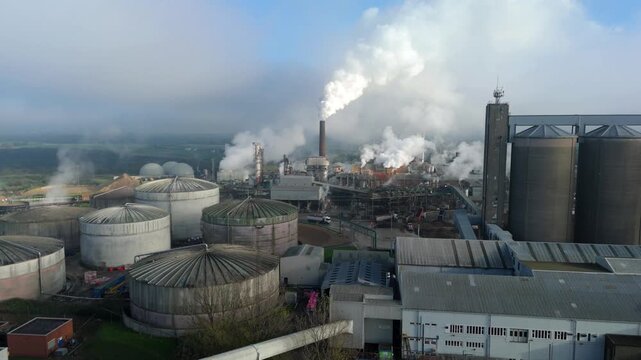 Aerial view of factory with tanks releasing smoke into the atmosphere, creating a stark contrast against the sky, Bury Saint Edmunds, England, United Kingdom.