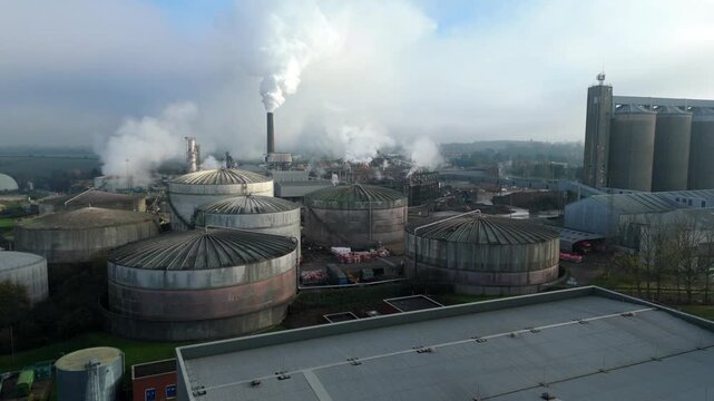 Aerial view of industrial plant releasing plumes of steam beside cylindrical silos and warehouses, Bury Saint Edmunds, England, United Kingdom.