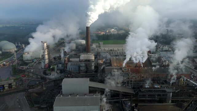 Aerial view of a sprawling industrial complex with chimneys expelling plumes of white smoke, contrasting against the landscape, Bury Saint Edmunds, England, United Kingdom.