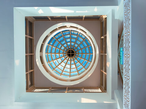 Looking up at a circular glass dome ceiling with geometric frames and blue-tinted panels creating a symmetrical architectural pattern.