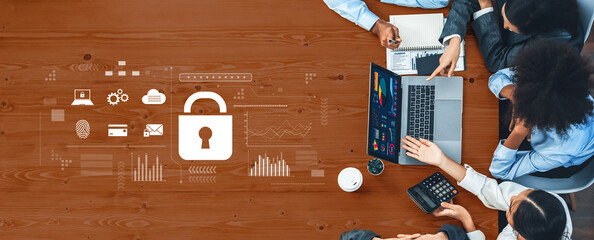 A diverse business team collaborates on a cybersecurity strategy during a meeting, utilizing a laptop and digital tools on a wooden table. Trope