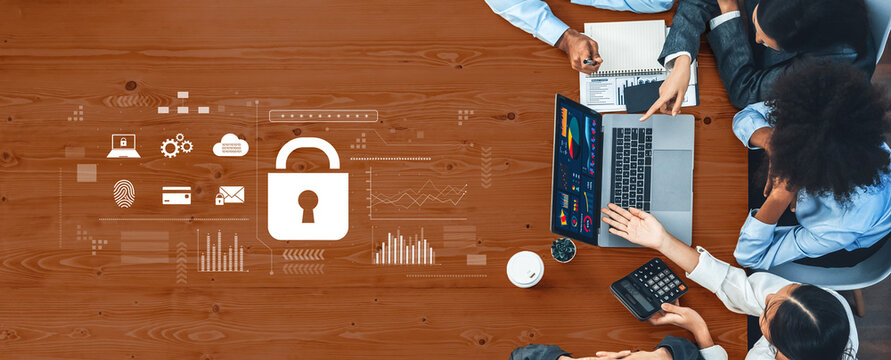 A diverse business team collaborates on a cybersecurity strategy during a meeting, utilizing a laptop and digital tools on a wooden table. Trope - Powered by Adobe