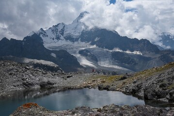 Majestic view of Batin North Peak (over 18,000 ft) near Matiltan village in the Hindu Raj Range, Pakistan. A lone trekker stands by an alpine tarn beneath towering glaciers and dramatic snow-clad peak