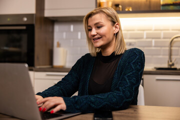 Woman working on a laptop in a modern kitchen during the day while smiling and engaged in her task
