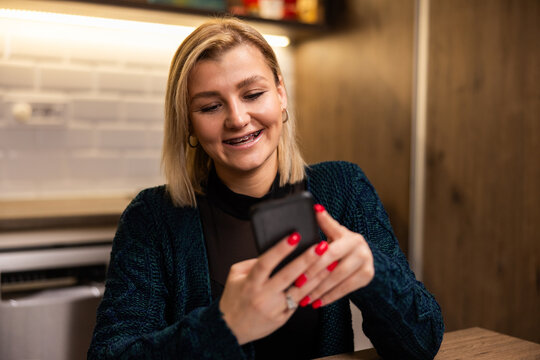 Woman enjoys using smartphone while sitting at a wooden kitchen table during relaxed indoor setting