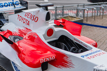 Obraz premium Toyota Formula 1 TF-108, vibrant red and white race car with Denso logo, viewed from angle, indoor exhibition setting, air intakes, vents, tiled floor, railing, even - Kyiv, Ukraine 10-10-2024