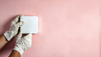 Hands wearing white gloves holding a modern network box against a smooth pink wall. Concept of advanced communication technology and installation, useful for articles on 5G, 6G,