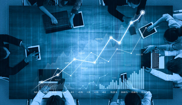 Aerial view of professionals working together on financial data analysis in a modern office. Multiple devices showcase graphs and statistical information. Scalp