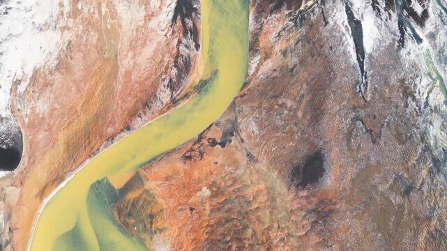 Aerial view of a glacial river carving through the stark landscape, with contrasting ochre earth and icy white snow creating a mesmerizing texture, Iceland.