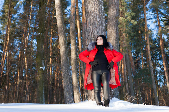 photo with a young woman in the winter forest. girl in a snowy park. in a red jacket on the banks of a frozen river. winter walk in nature. Cold season. Beautiful girl, sunny day.