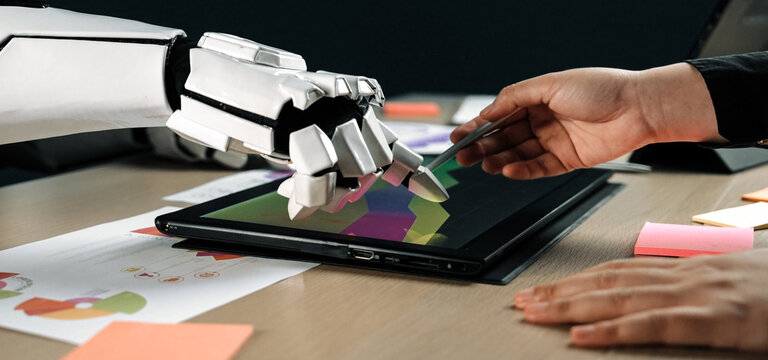 A robotic hand and a human hand engage in collaborative digital art creation on a touchscreen tablet in a modern office setting, showcasing innovation and creativity.Noogenesis