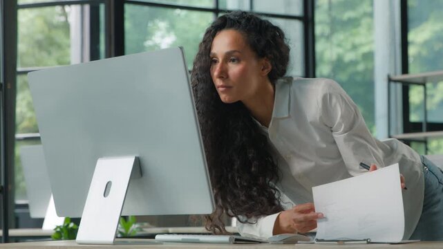 Hispanic business woman typing computer cyberspace checking document in office standing businesswoman female girl with papers and internet technology review summary finance data working sales analyze