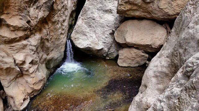 Overhead perspective of a secluded waterfall cascading into a serene turquoise pond, nestled among jagged rock structures