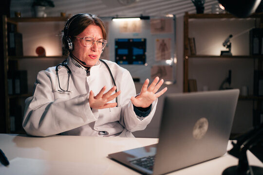 Female doctor or nurse in uniform wear headset say no thanks use laptop computer talking on video call with patient in hospital during night shift. Consulting, telemedicine and therapy