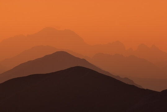 View of layered mountain silhouettes fading into the hazy orange sky, creating a serene and ethereal landscape, Jamnik, Zilina Region, Slovakia.