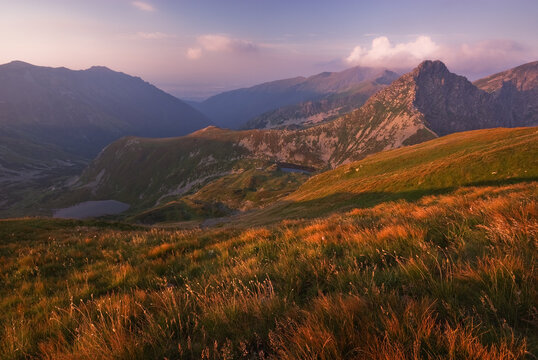 View of golden light sweeping across the grassy slopes and rugged peaks under a soft sky, Rakon, Zilina Region, Slovakia.