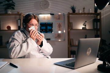 Female doctor in uniform wear headset sniff money cash use laptop computer talking on video call with patient in hospital during night shift. Consulting, telemedicine and therapy