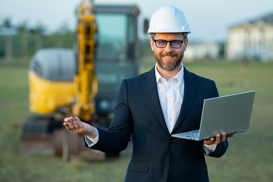 Architect at a construction site. Architect man in helmet and suit at modern home building construction. Architect with a safety vest and suit. Confident architect standing at house background.