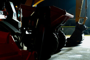 Industrial worksite at night featuring a multi-wheel compaction machine beside an excavator bucket, highlighting the operational demands and business activity of modern construction process