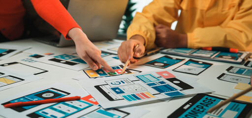 A dynamic design session showcasing team collaboration around a table with mobile application prototypes and sketches, highlighting creativity and strategic planning. SACTR