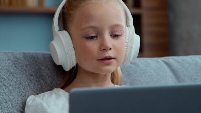 Caucasian relaxed cute child girl listening music in headphones kid daughter listen song at home with laptop closed eyes enjoying song singing with computer fun sing musical audio in internet dance