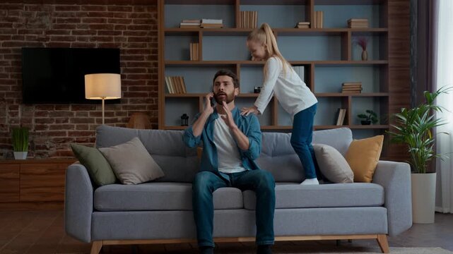 Family trouble at home stressed father trying talking phone daughter jumping disturb business man talk call distant work quarantine little noisy hyperactive kid girl child jump on couch bad behavior