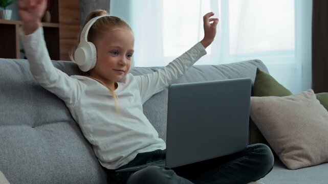 Caucasian smiling pupil child girl communicate video call with laptop hello gesture e-learning daughter in headphones kid schoolgirl with computer talking with online chat virtual conference at home