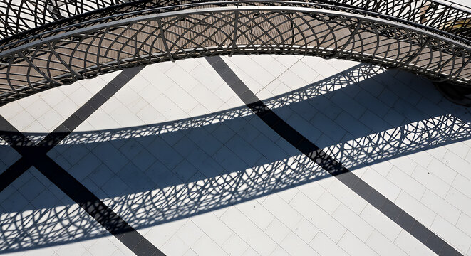Intricate metal archway creates striking geometric shadows on a textured concrete surface outdoors - Powered by Adobe
