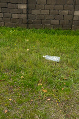 Plastic bottle discarded on grass near stone wall in a public space during daylight
