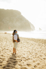 Traveler stands barefoot on a sunlit beach, gazing at the bright shoreline and rocky cliffs, capturing a calm, reflective coastal moment. Stock photo