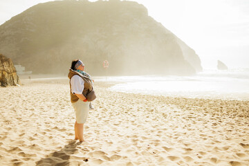 Traveler stands barefoot on a sunlit beach, gazing at the bright shoreline and rocky cliffs,...
